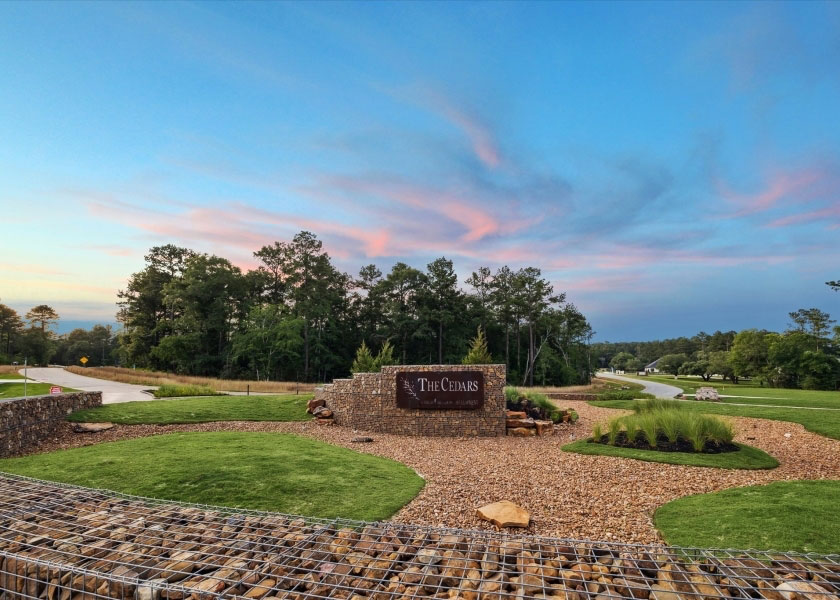 Landscaped stone entrance sign for The Cedars residential development at sunset.