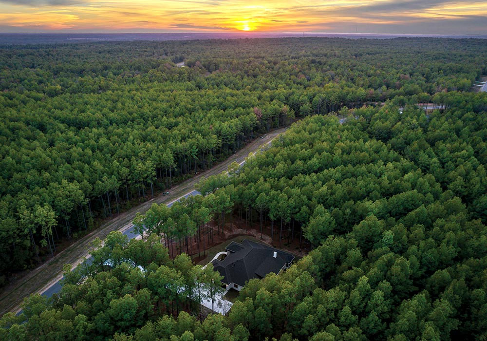 Aerial view of a custom home nestled in a secluded forest at sunset.