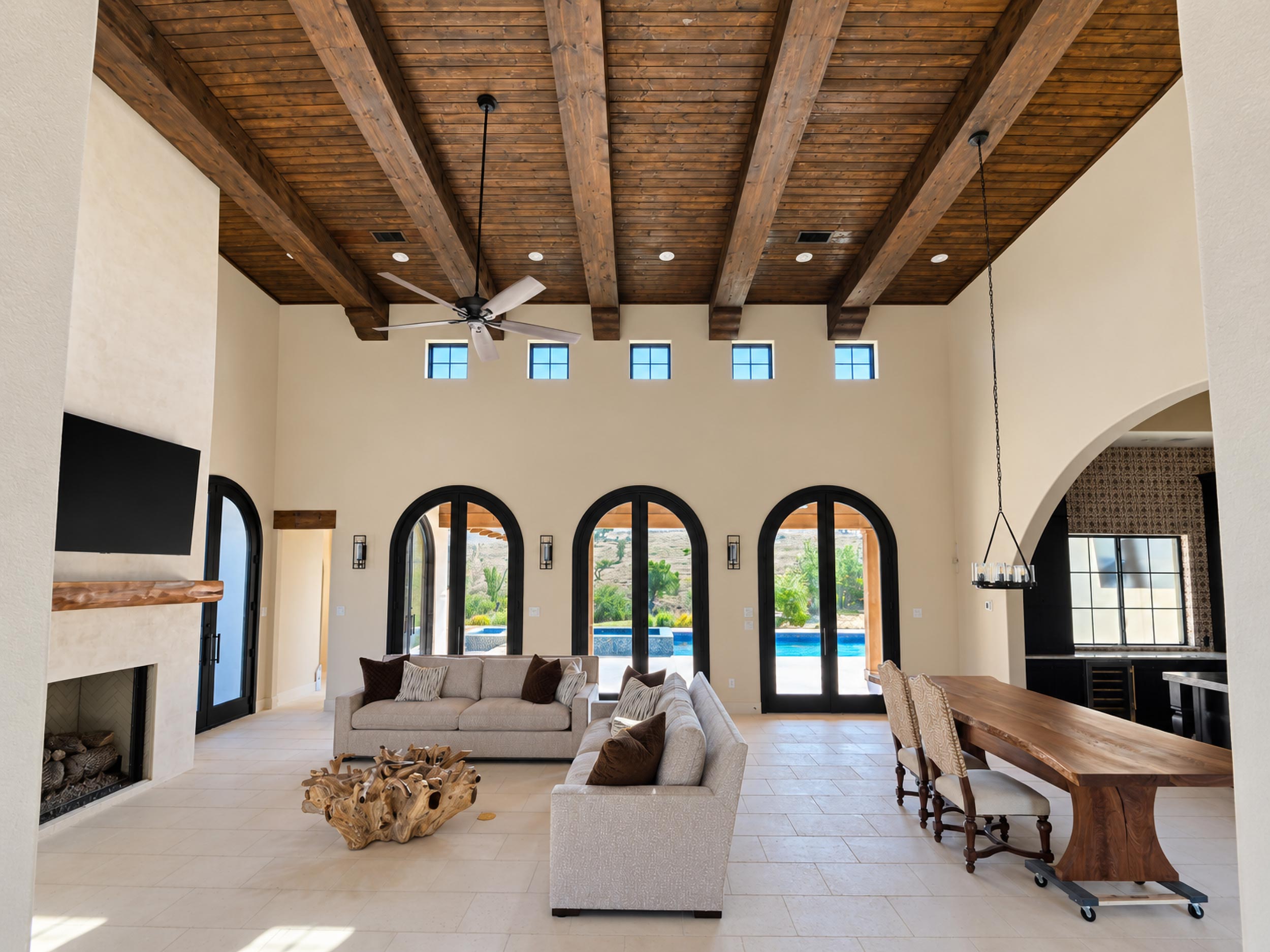 Custom home great room with stained wood beam ceiling, arched French doors and pool view